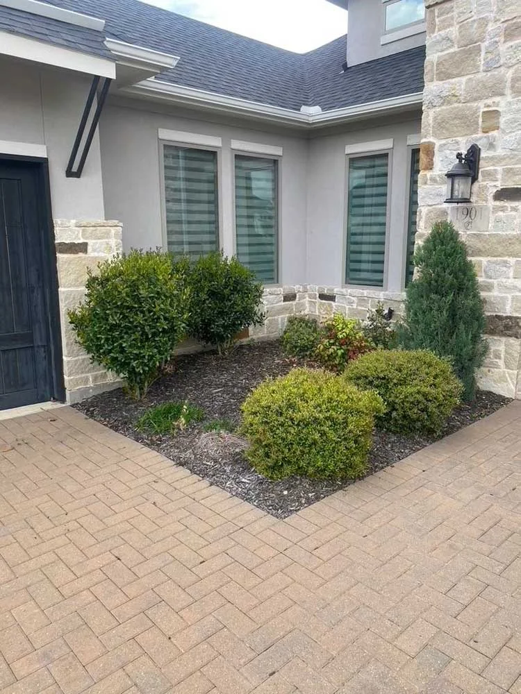 A North Dallas home with a brick driveway and landscaped bushes.